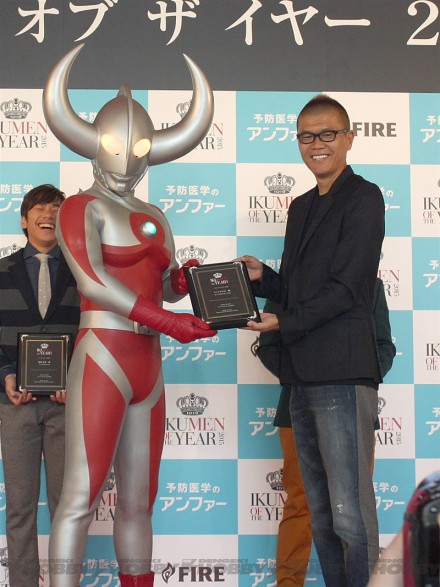 ▲おちまさと実行委員長から楯を受け取るウルトラの父。織田信成さんもそのようすを笑顔で見ています。